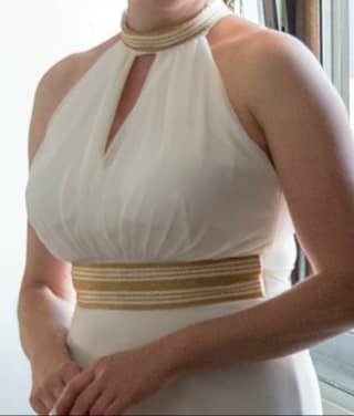 A close-up of a white halter-neck wedding dress featuring a custom handmade woven belt and matching collar detail in elegant gold and white stripes, created by Ergastini.