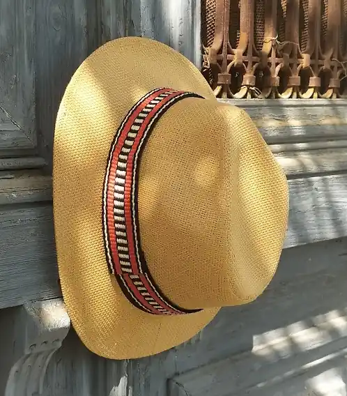 A yellow straw hat hanging on a weathered wooden door, adorned with a custom band woven by Zoe on an inkle loom.